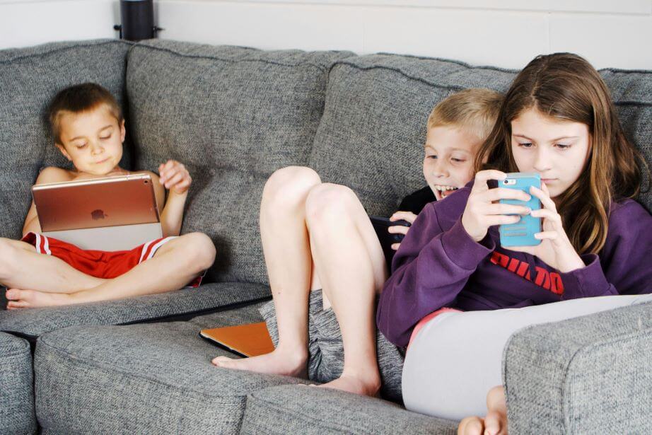 3 children sitting on couch playing on their digital devices